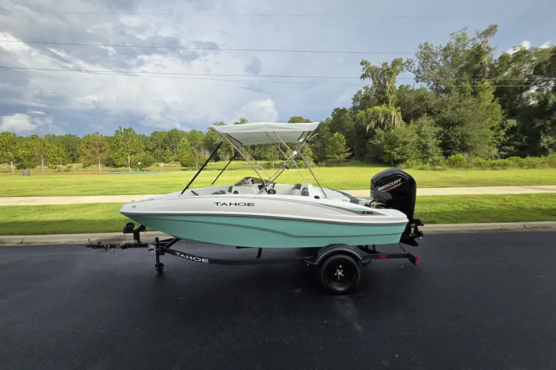 The Image of 2027 Tahoe T16 boat on trailer, parked outdoors with lush greenery background. - 0