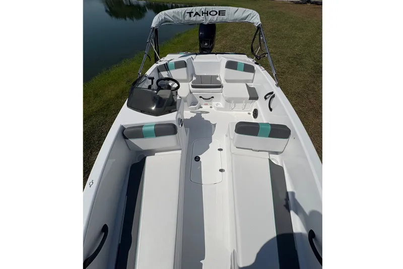 Slide: The Image of 2027 Tahoe T16 boat interior with seating and steering, parked near a lake. - 10