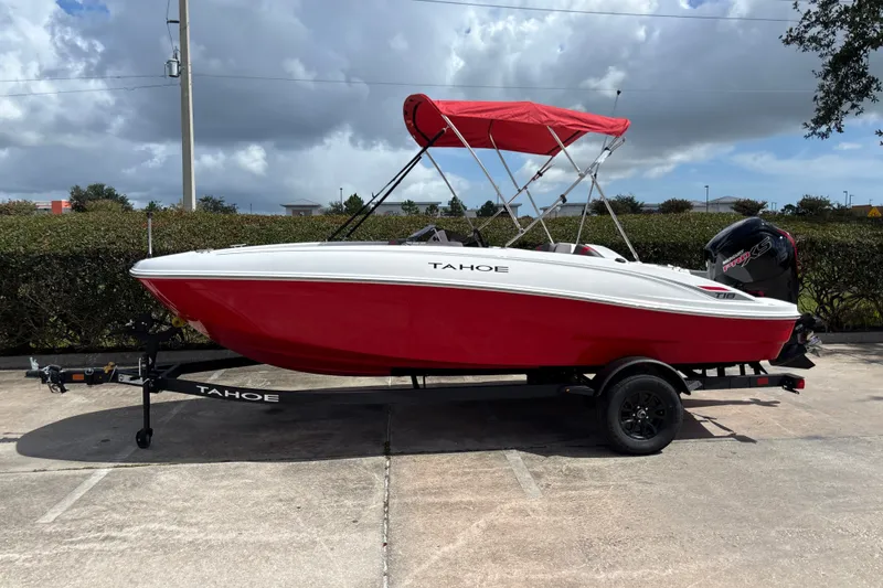 The Image of 2027 Tahoe T18 boat with red hull and canopy on a trailer, parked outdoors. - 0