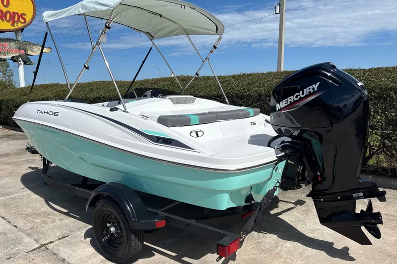 Slide: The Image of 2027 Tahoe T16 boat with Mercury engine, parked on trailer under sunny sky. - 2