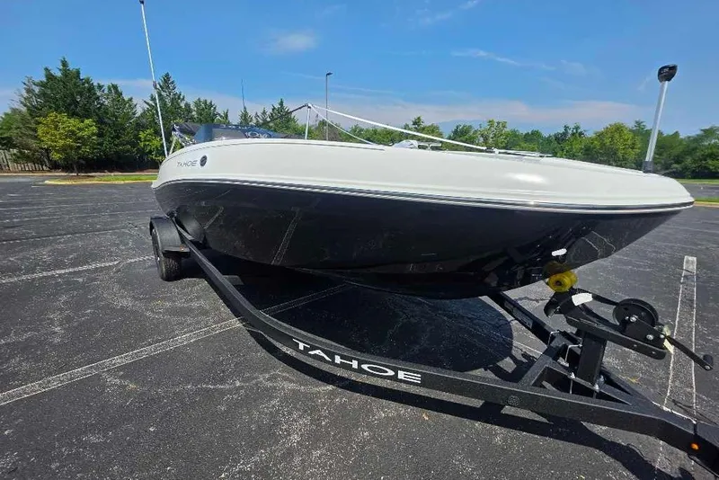 Slide: The Image of 2027 Tahoe T18 boat on trailer in parking lot, surrounded by trees under clear sky. - 7