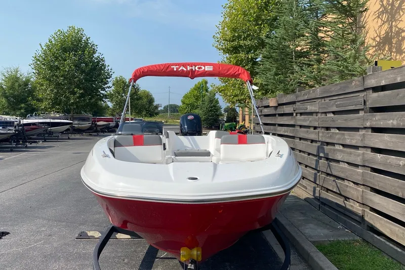 Slide: The Image of 2027 Tahoe T18 boat with red canopy, parked outdoors near wooden fence. - 3