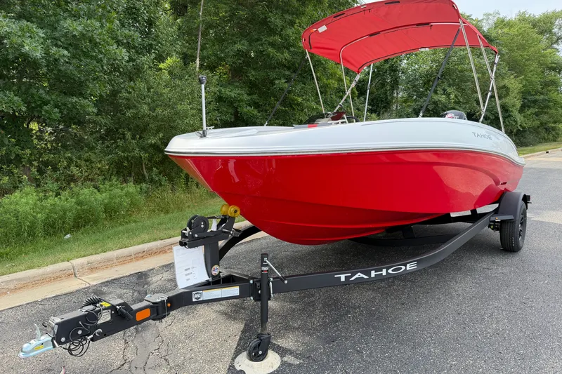 Slide: The Image of Red 2027 Tahoe T18 boat on trailer with canopy, parked near lush greenery. - 2