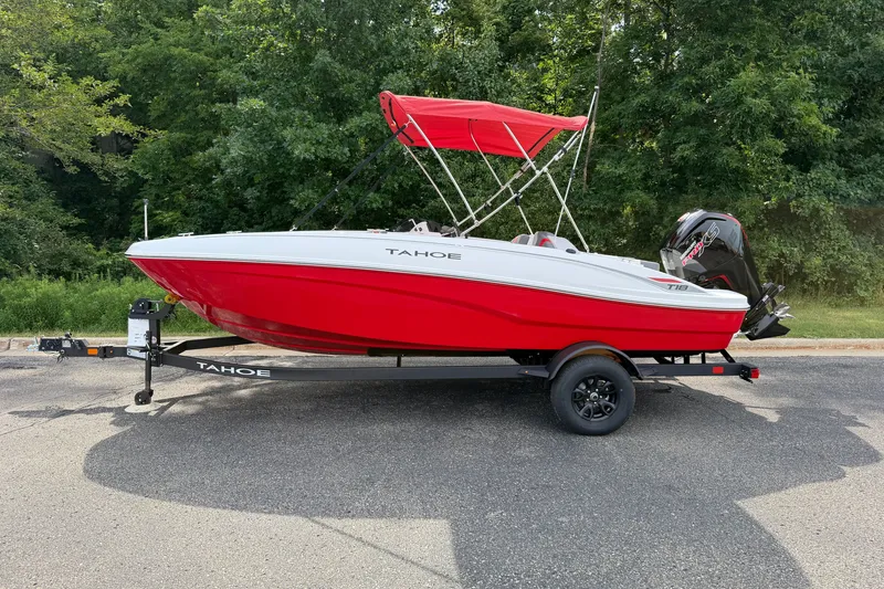 The Image of 2027 Tahoe T18 boat with red hull and canopy on a trailer, parked outdoors. - 0
