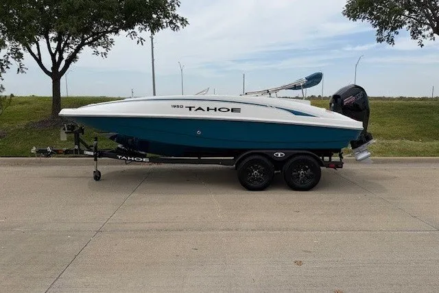The Image of 2027 Tahoe 1950 boat on trailer, parked on a paved road with trees in the background. - 97