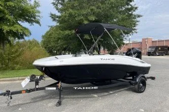 Slide: The Image of 2027 Tahoe T16 boat on trailer, parked outdoors with trees and building in background. - 1