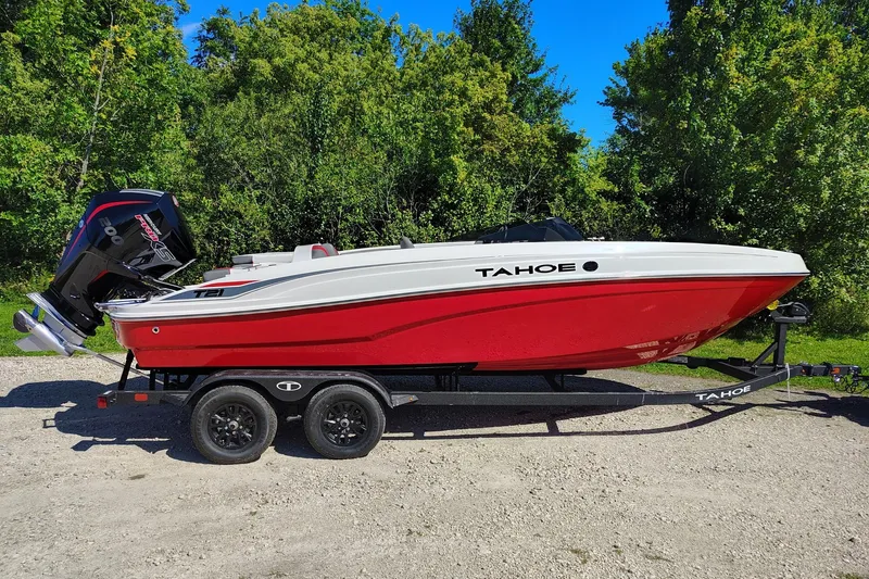 The Image of 2027 Tahoe T21 boat in red and white on a trailer, surrounded by greenery. - 0