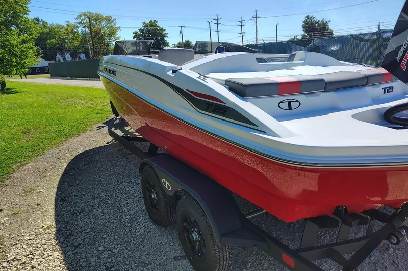 Slide: The Image of 2027 Tahoe T21 boat on trailer, red and white design, parked on gravel path. - 2