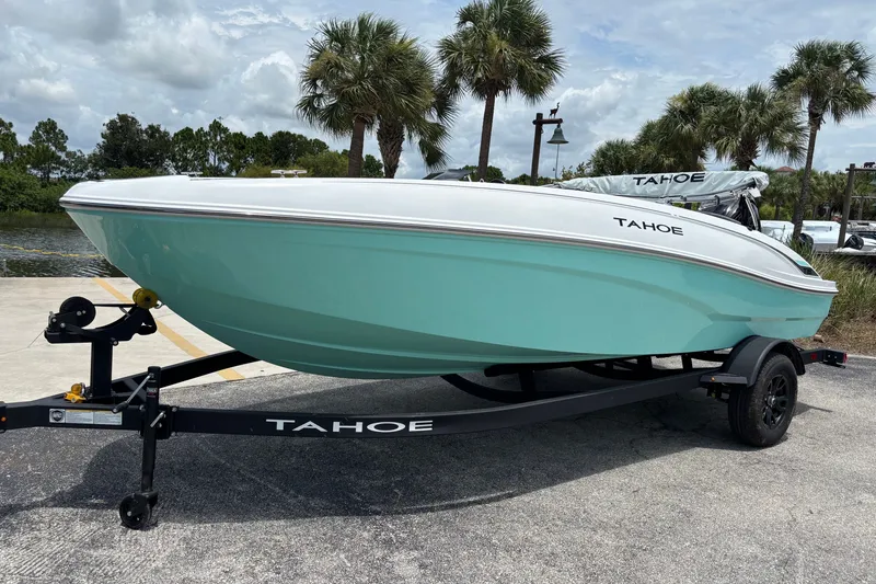 Slide: The Image of 2027 Tahoe T18 boat on trailer, parked near palm trees under a cloudy sky. - 2