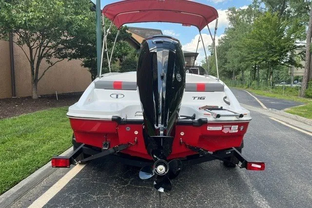 Slide: The Image of 2027 Tahoe T16 boat with red and white design, parked on a street with a canopy. - 2