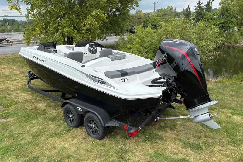 Slide: The Image of 2027 Tahoe T21 boat on trailer, parked on grass near a pond, showcasing sleek design. - 2