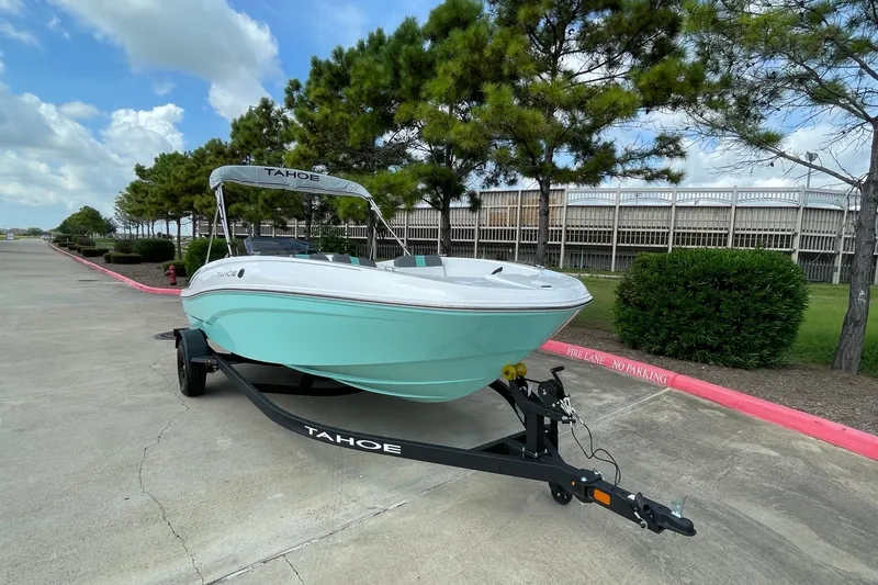 Slide: The Image of 2027 Tahoe T18 boat on trailer, parked near trees under a blue sky. - 2