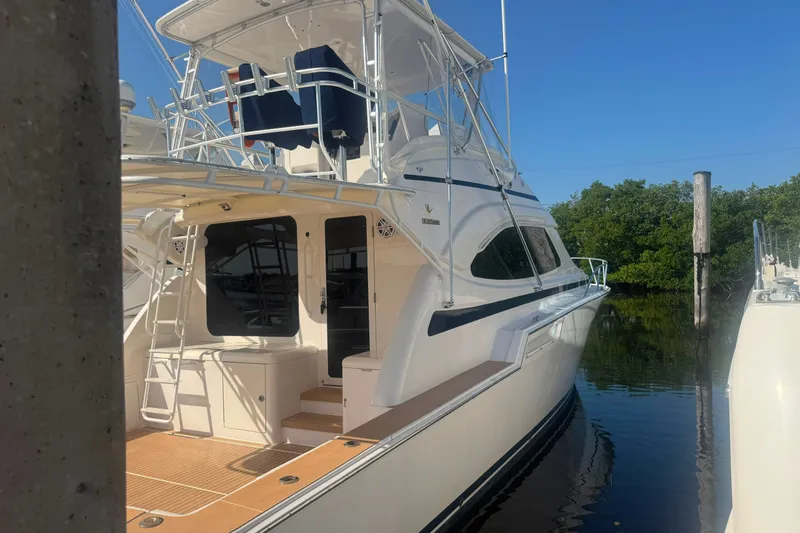 Slide: The Image of 2003 Bertram 450 Convertible yacht docked by lush greenery under clear blue skies. - 1