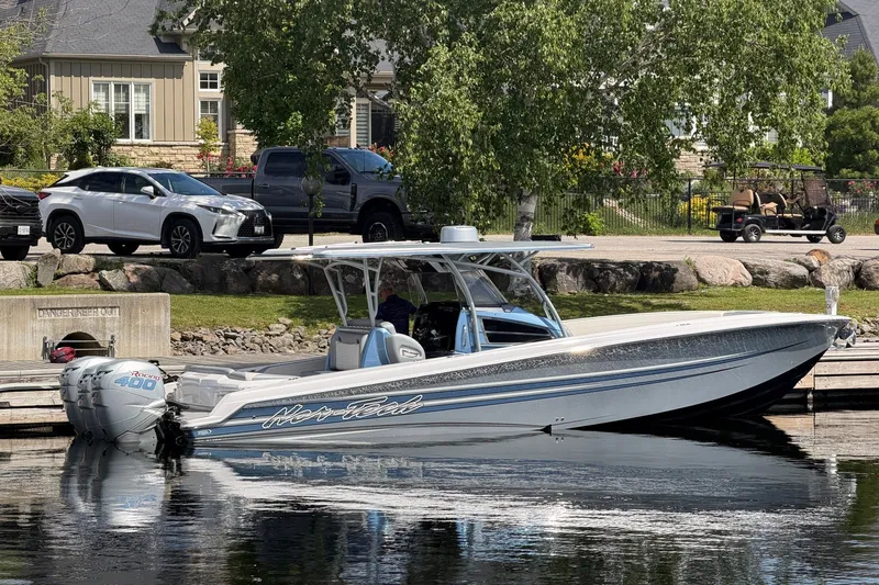 The Image of 2022 Nor-Tech 340 Sport boat docked near waterfront homes and parked vehicles. - 1