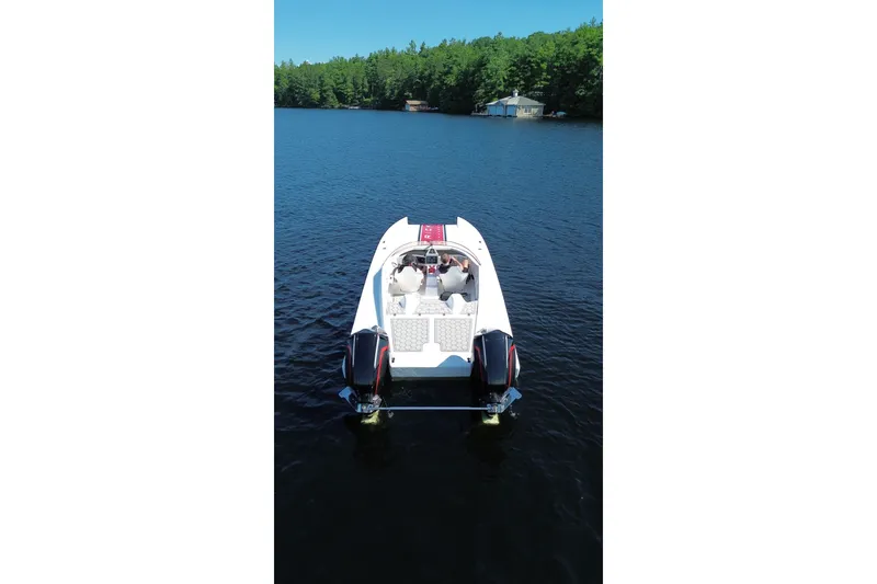 Slide: The Image of 2024 Trick 23 Widebody boat on a serene lake with lush green shoreline. - 2