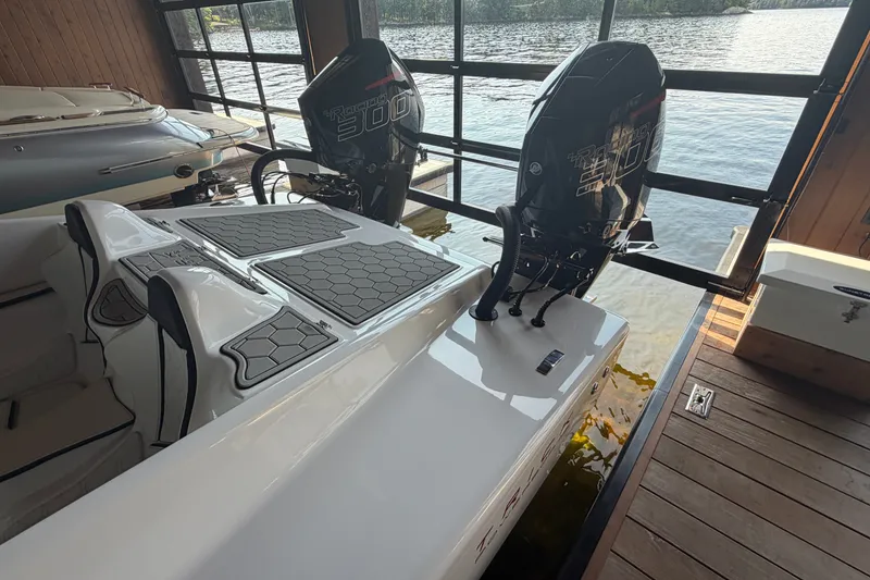 Slide: The Image of 2024 Trick 23 Widebody boat with dual outboard motors in a lakeside boathouse. - 19