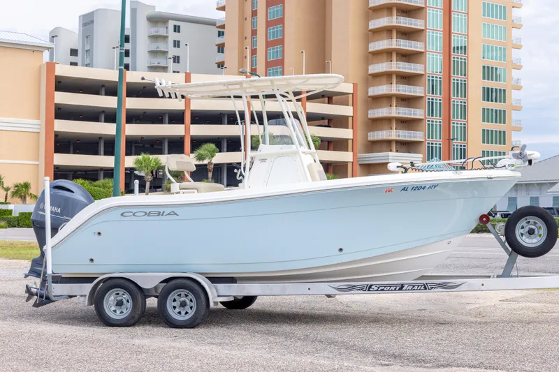 The Image of 2016 Cobia 201 Center Console boat on trailer, parked near modern buildings. - 0