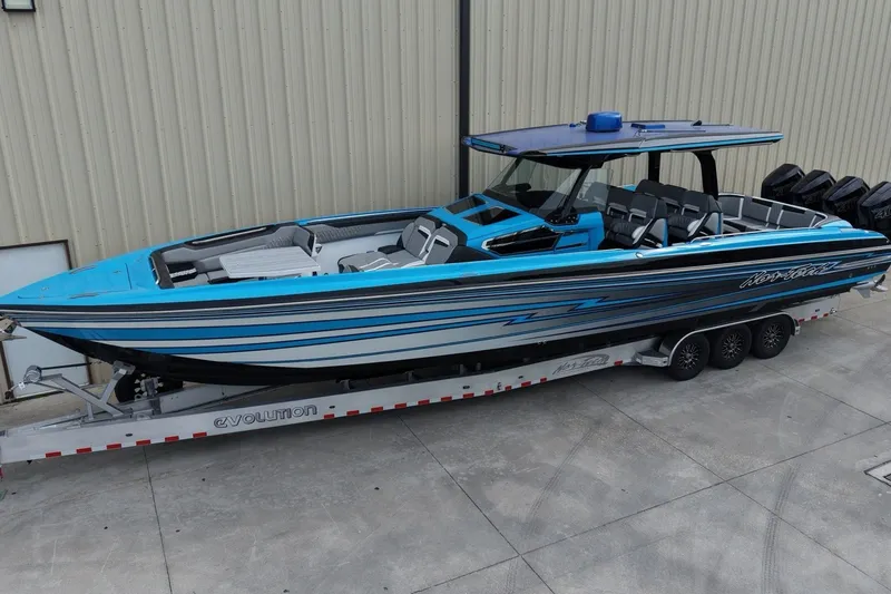 The Image of 2027 Nor-Tech boat in blue and black on a trailer, parked outside a building. - 1