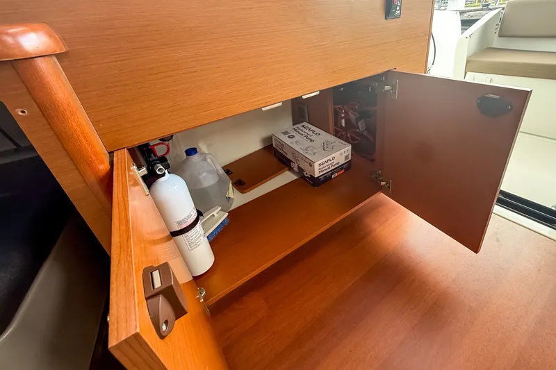 Slide: The Image of Open wooden cabinet on Jeanneau Merry Fisher 855 boat, showing storage items and fire extinguisher. - 17