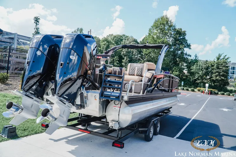 Slide: The Image of 2025 Barletta L25MAT pontoon boat on trailer, featuring dual engines, parked outdoors. - 3