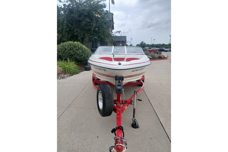 Slide: The Image of 2003 Larson SEi 180 boat on red trailer, parked on a paved area. - 2