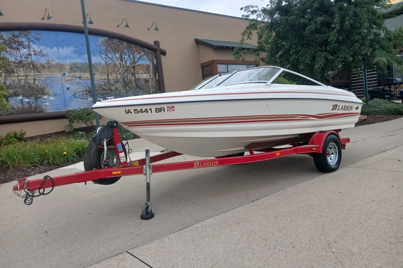 Slide: The Image of 2003 Larson SEi 180 boat on red trailer, parked outdoors near mural. - 3
