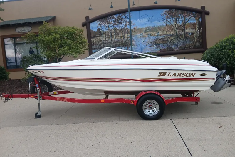 The Image of 2003 Larson SEi 180 boat on red trailer, parked outdoors near a mural. - 1