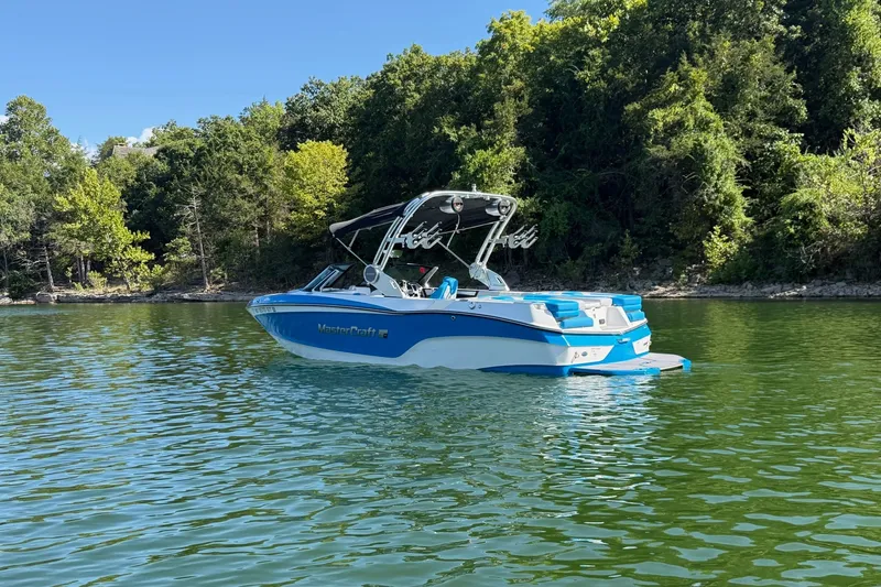Slide: The Image of 2023 MasterCraft XT23 boat on a serene lake with lush green forest backdrop. - 41