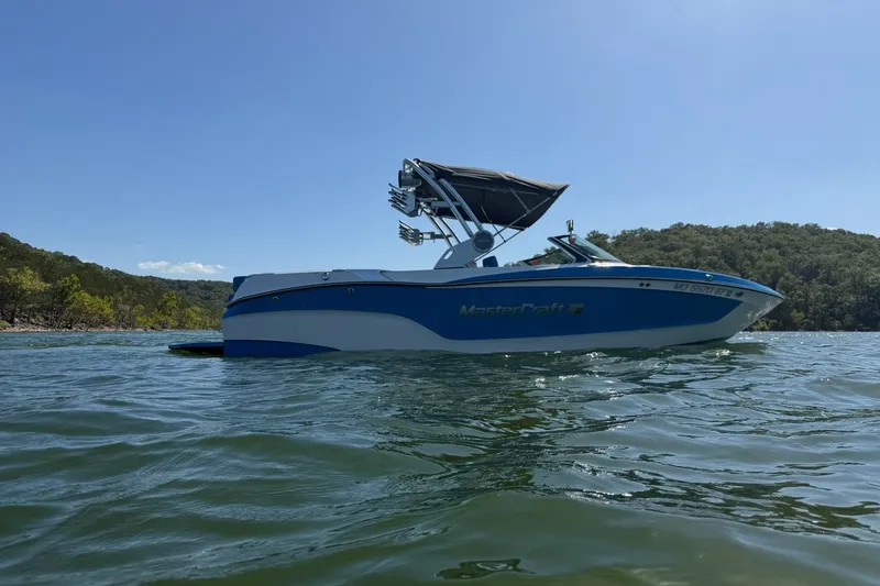 Slide: The Image of 2023 MasterCraft XT23 boat on a serene lake with lush green hills. - 38