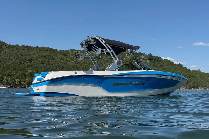 Slide: The Image of 2023 MasterCraft XT23 boat on a lake with lush green shoreline. - 37
