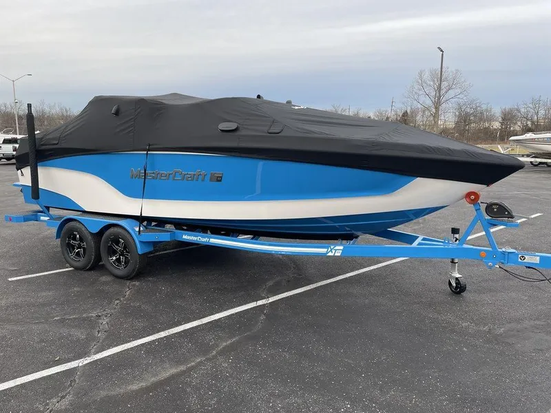 Slide: The Image of A blue and white 2023 MasterCraft XT23 boat on a trailer with a black cover. - 47