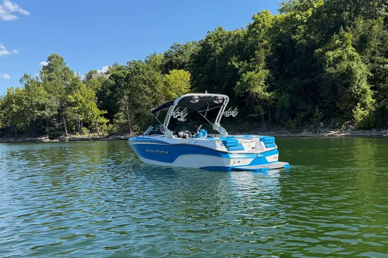 Slide: The Image of 2023 MasterCraft XT23 boat on a serene lake with lush green trees. - 42