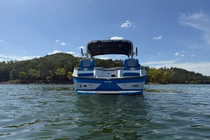 Slide: The Image of 2023 MasterCraft XT23 boat on a serene lake with forested shoreline. - 40