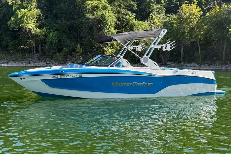 The Image of 2023 MasterCraft XT23 boat on a serene lake with lush green trees. - 0