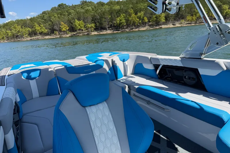 Slide: The Image of 2023 MasterCraft XT23 boat interior with blue and white seating on a lake. - 26