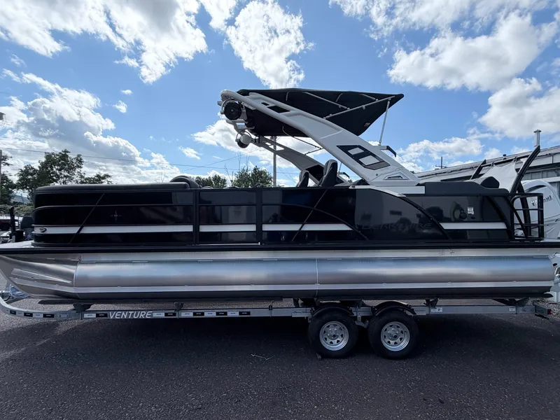 The Image of A modern tritoon with black railing and sleek white canopy, sitting on a trailer. - 1