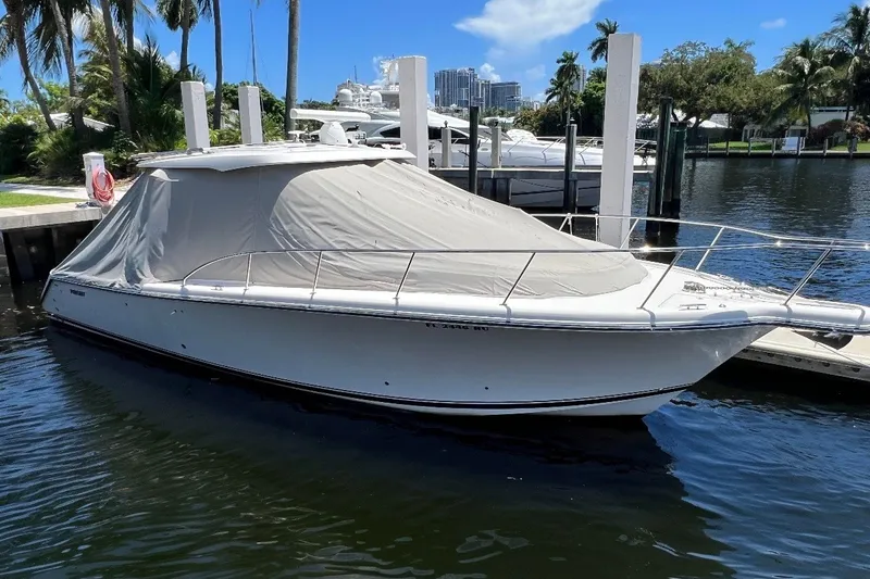 Slide: The Image of 2018 Pursuit OS 385 Offshore boat docked with cover, surrounded by palm trees. - 2