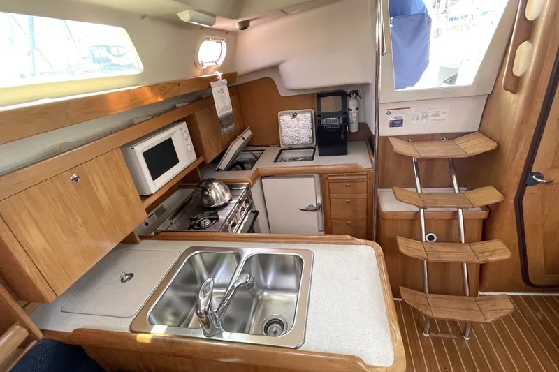Slide: The Image of 2004 Catalina 350 yacht interior kitchen with wooden cabinetry, stainless steel sink, and appliances. - 3