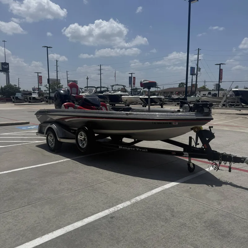 Slide: The Image of A 2019 Ranger Z518 boat on a trailer in a parking lot. It features red seats and fishing rod holders. - 6