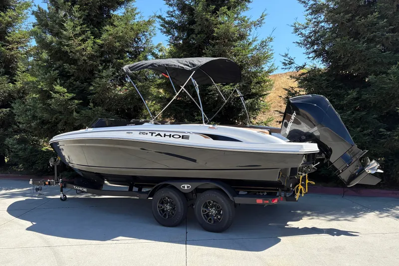 Slide: The Image of 2027 Tahoe 210 S boat on trailer, parked outdoors with trees in background. - 5