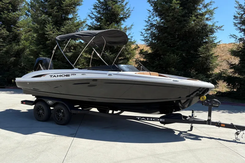 Slide: The Image of 2027 Tahoe 210 S boat on trailer, parked outdoors with trees in background. - 2