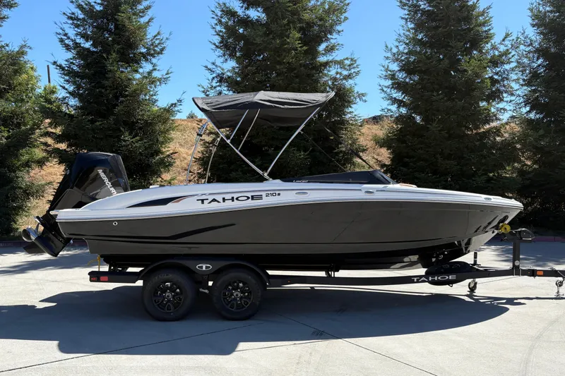 The Image of 2027 Tahoe 210 S boat on trailer, parked outdoors with trees in background. - 0