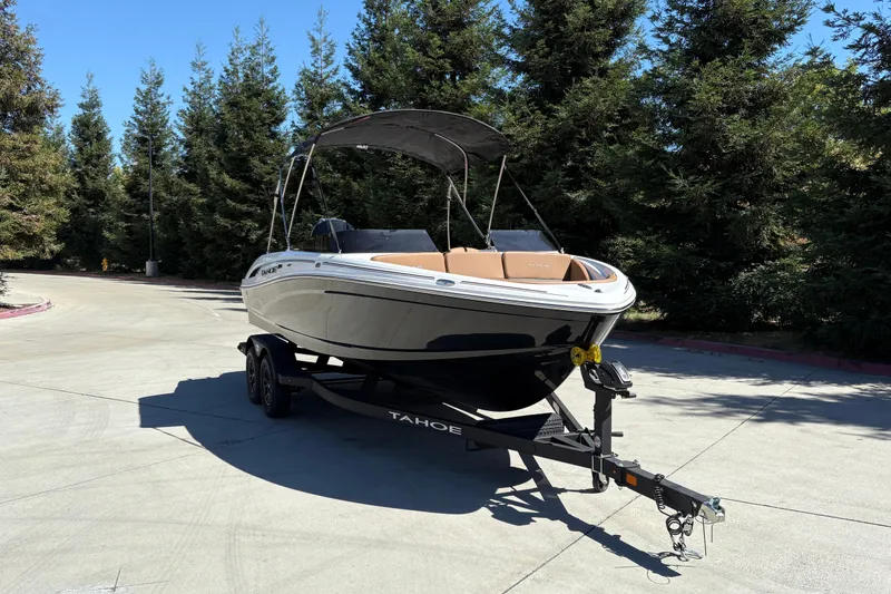 Slide: The Image of 2027 Tahoe 210 S boat on trailer, parked outdoors with trees in background. - 6