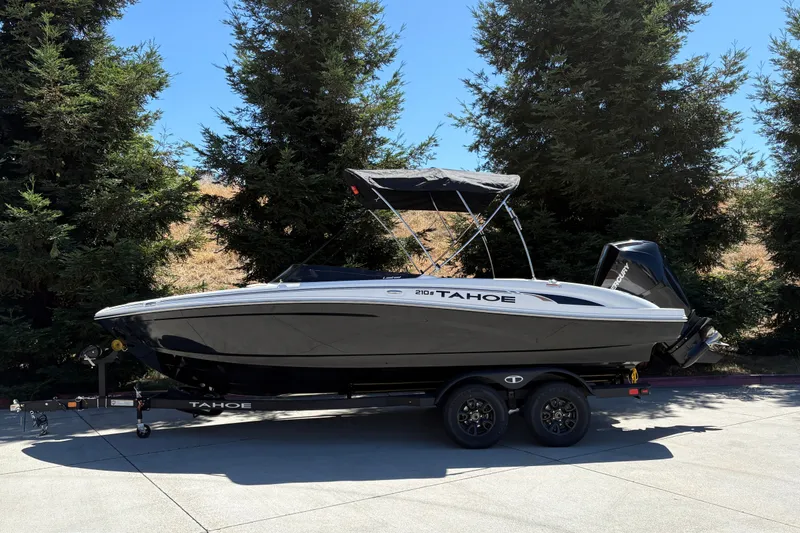 Slide: The Image of 2027 Tahoe 210 S boat on trailer, parked outdoors with trees in background. - 1