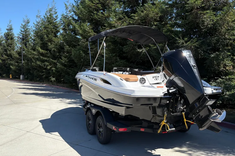 Slide: The Image of 2027 Tahoe 210 S boat on trailer, parked near trees, with outboard motor. - 10