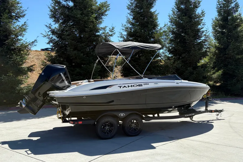 Slide: The Image of 2027 Tahoe 210 S boat on trailer, parked outdoors with trees in background. - 3