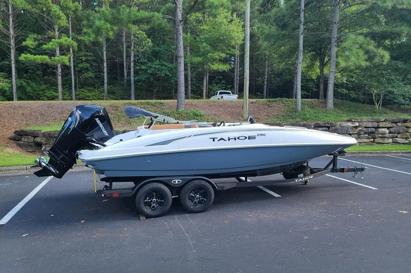 The Image of 2027 Tahoe 2150 boat on trailer in wooded parking area. - 0