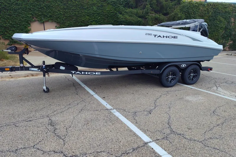 Slide: The Image of 2027 Tahoe 2150 boat on trailer in parking lot, surrounded by greenery. - 2