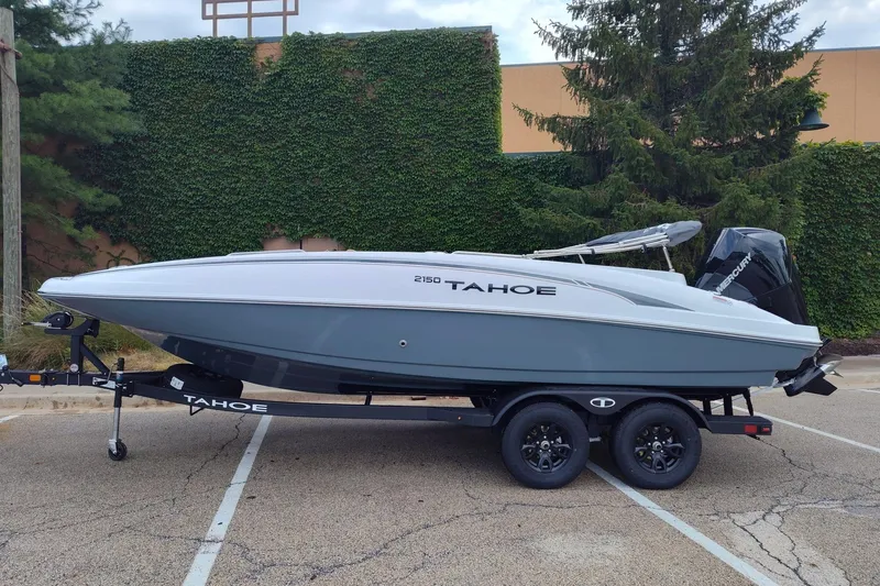 The Image of 2027 Tahoe 2150 boat on trailer, parked outdoors with greenery background. - 0