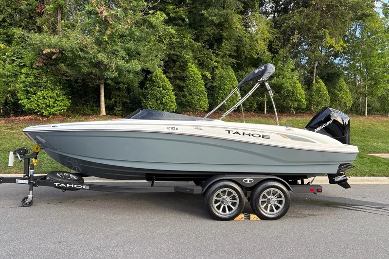 The Image of 2027 Tahoe 210 S boat on trailer, parked on road with lush green background. - 0